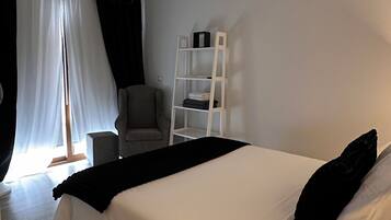 Ein modernes Schlafzimmer mit einem großen Bett, einem Sessel, einer Leiterregal und transparenten Vorhängen.