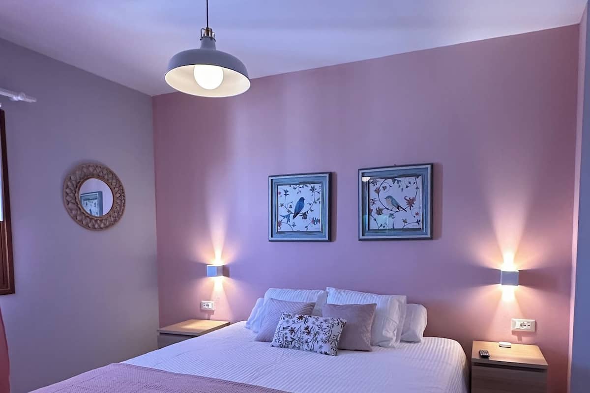 Een slaapkamer met een groot bed, twee wandlampen, een plafondventilator en twee ingelijste foto's aan de muur.