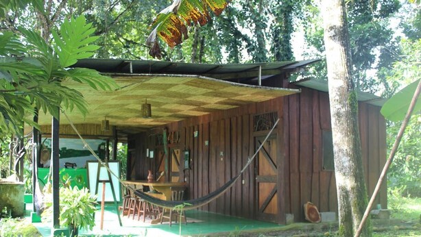 A rustic wooden cabin with a covered porch, a hammock, and a dining area. - Finca Guarumo - Hostel (Las Horquetas)