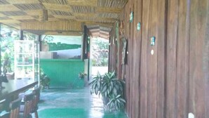 A covered outdoor area with a green floor, wooden walls, and a thatched roof. - Finca Guarumo - Hostel (Las Horquetas)