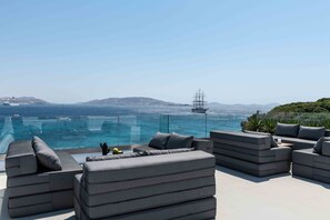 Une terrasse sur le toit, dotée de canapés gris modernes et d’une balustrade en verre offrant une vue sur la mer.