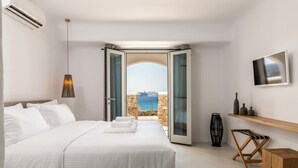 A bedroom with a large bed, a view of the sea through an open door, a TV on the wall, and a wooden bench. - Obsession Mykonos (Mykonos)