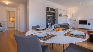 A modern dining area with a round table set for four, surrounded by chairs. There are shelves with decorative items and a television in the background. - Downtown Apartment Santa Justa (Lisboa)