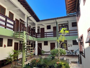 A multi-story building with a green and white exterior, a central staircase, and a small courtyard with plants and outdoor furniture. - Pousada Paraíso Ilha Grande (Angra dos Reis)