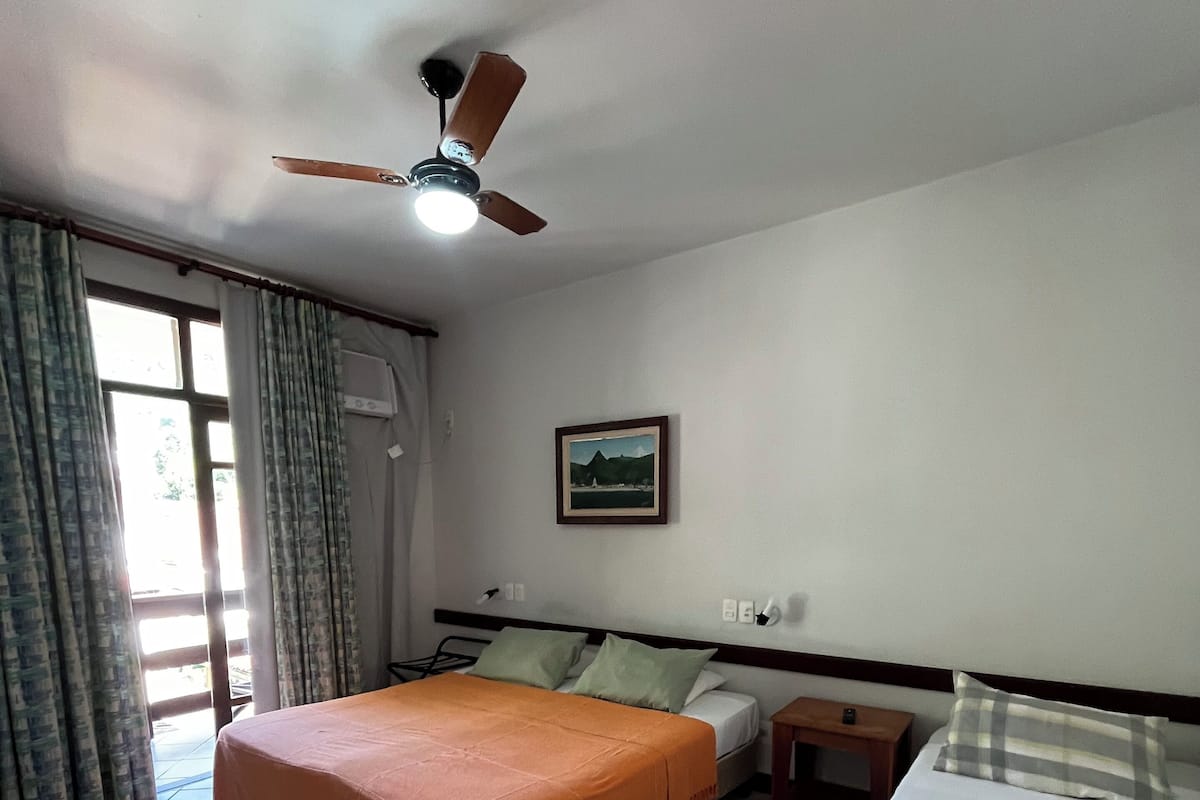 Une chambre d’hôtel équipée d’un lit, d’un bureau, d’une chaise, d’un ventilateur de plafond et d’une fenêtre avec des rideaux.