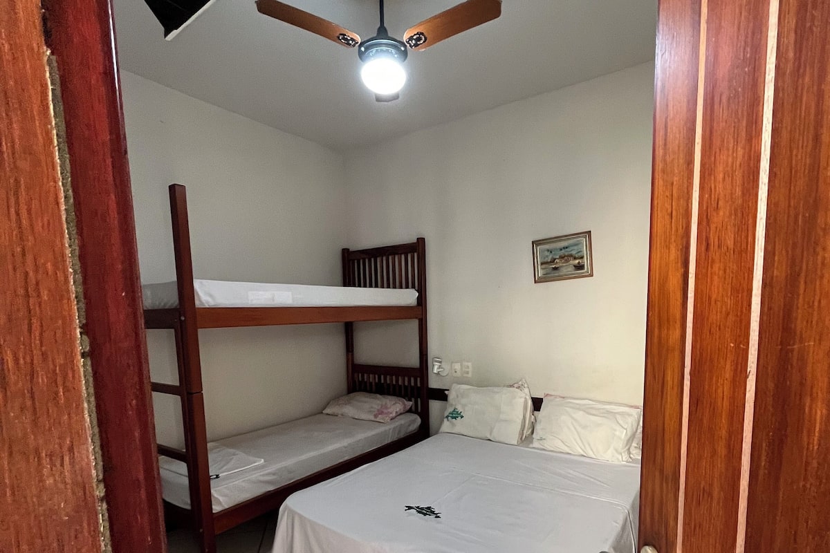 Une chambre avec un lit superposé, un lit simple, un ventilateur de plafond et un luminaire fixé au mur.