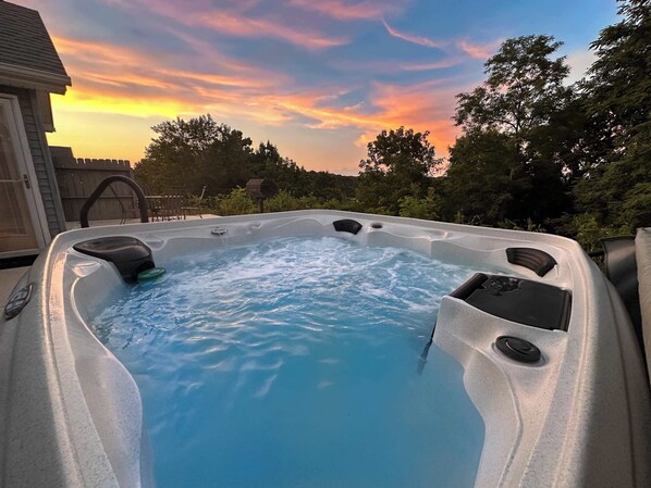 A hot tub with a waterfall feature, surrounded by trees and a wooden fence.