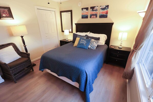 Un dormitorio con cama, una silla, mesita de noche, lámpara y puerta.