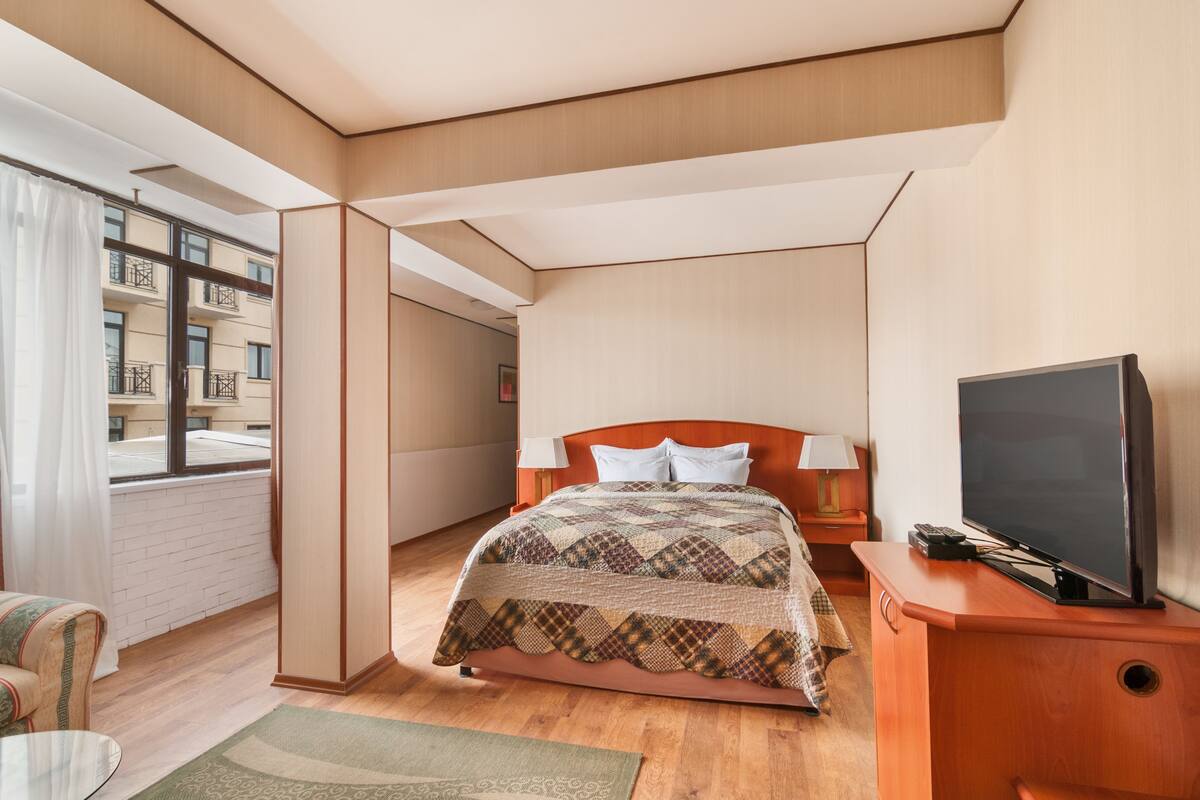 A modern hotel room with a large bed, a TV, and a view of the city.