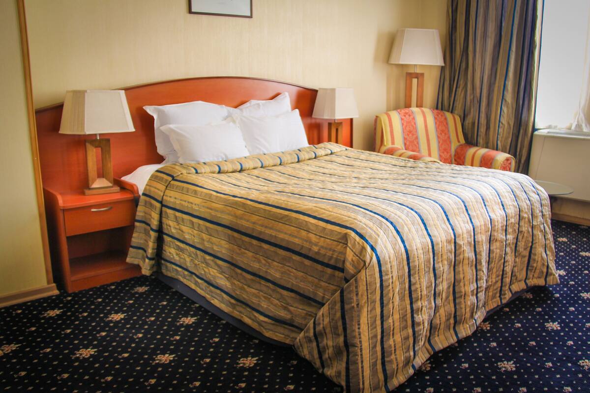 A hotel room with a bed, two bedside tables, a chair, and a window with curtains.