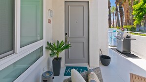 Une entrée propre et moderne, avec une porte grise, un pot de fleurs, un paillasson et un barbecue sur la terrasse.