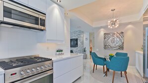 Une cuisine moderne équipée d’un four encastré, d’un four à micro-ondes et d’une cuisinière à gaz. On y trouve également un coin repas avec une table et des chaises.