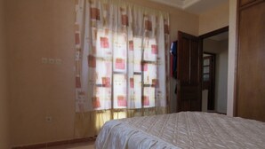 A bedroom with a bed, a window with a patterned curtain, and a door leading to another room. - Villa 400m2 with swimming pool 10 min from the beach tifnit (Agadir)