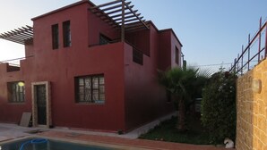 A red two-story house with a swimming pool in the foreground. - Villa 400m2 with swimming pool 10 min from the beach tifnit (Agadir)
