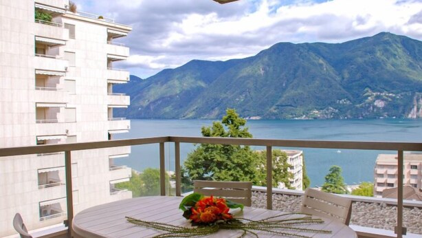 Un balcon avec une table et des chaises, donnant sur un lac et des montagnes.