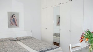 Une chambre à coucher avec un lit, un miroir, une table sur laquelle est posé un vase de fleurs et un tableau accroché au mur.