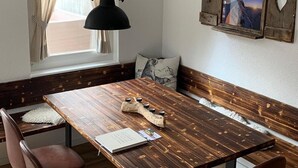 Une table de salle à manger en bois, surmontée d’un luminaire suspendu noir, un banc avec un coussin et un cadre photo fixé au mur.