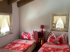 Een kamer met twee bedden, elk met rood-wit geruit beddengoed, een rode lamp op een nachtkastje en een raam met gordijnen.