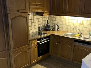 A kitchen with wooden cabinets, a tiled backsplash, a stove, an oven, a sink, and a coffee maker.