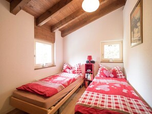 A bedroom with two single beds, a bookshelf, and a window.