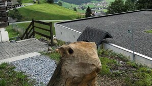 Une vue d’une région montagneuse, avec un bâtiment doté d’un toit en pente et d’une clôture en bois.