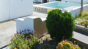 Un edificio blanco con piscina, un pequeño jardín con flores y un césped bien cuidado.