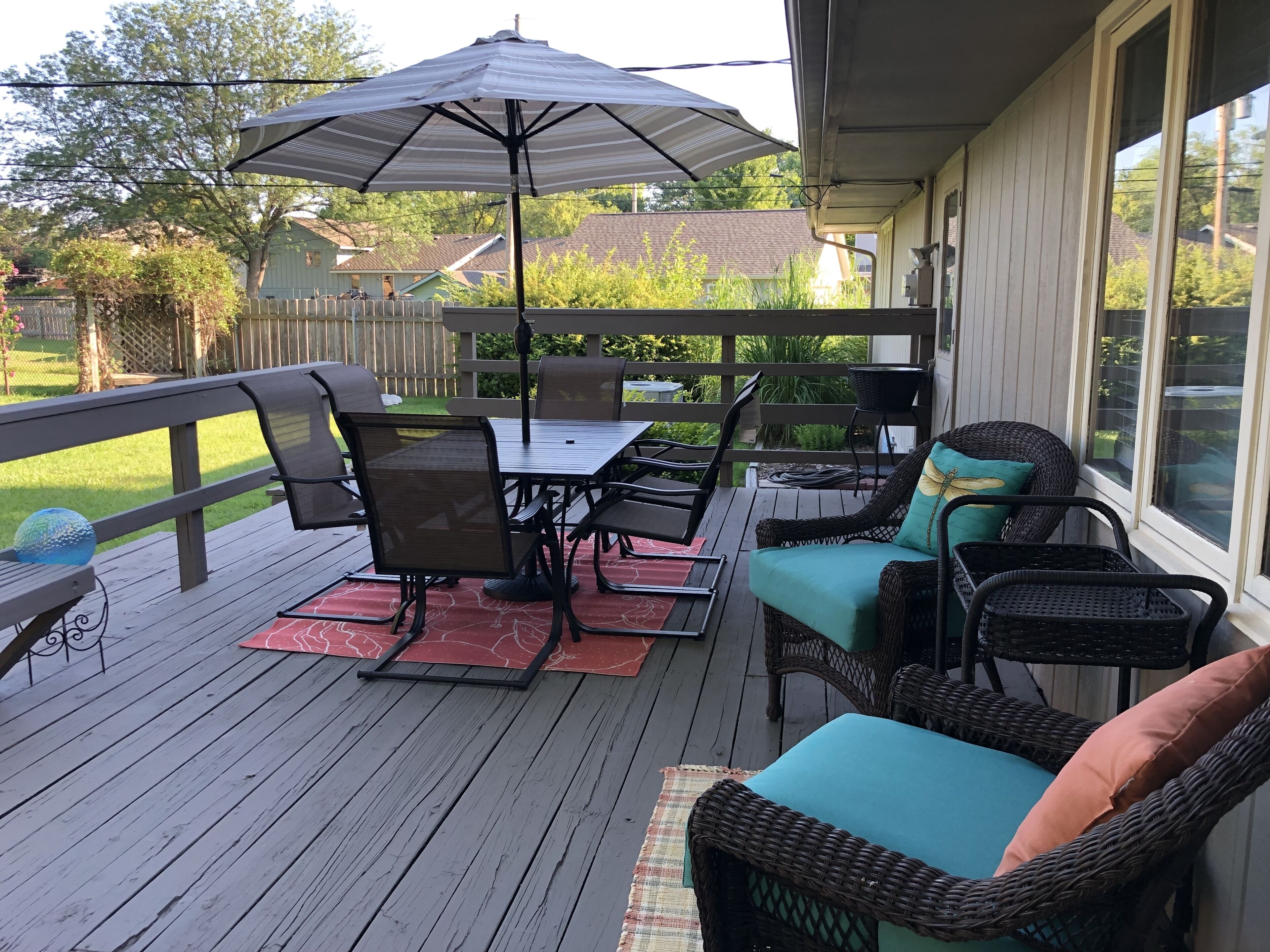 Een overdekt terras met een tafel, stoelen en een rieten bank, plus een parasol.