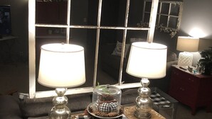 Una habitación con una mesa de estilo antiguo que incluye dos lámparas, un centro decorativo y un espejo con marco desgastado.