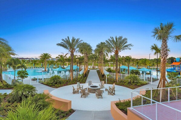 A resort pool area with a circular seating arrangement, palm trees, and a clear sky.