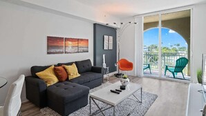 Ein modernes Wohnzimmer mit einem dunkelgrauen Sofa, einem weißen Couchtisch und einem Balkon mit grünen Stühlen.