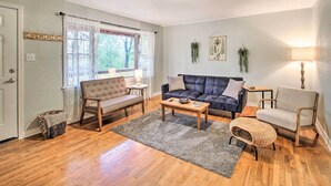 A living room with a sofa, armchair, and coffee table. There is a window with curtains, a lamp, and a plant on the wall. - Centrally Located Hot Springs Home w/ Deck! (Hot Springs)