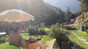 A person dining at an outdoor table with a view of a mountainous landscape. - Atlas Tigmi (Sti Fadma)
