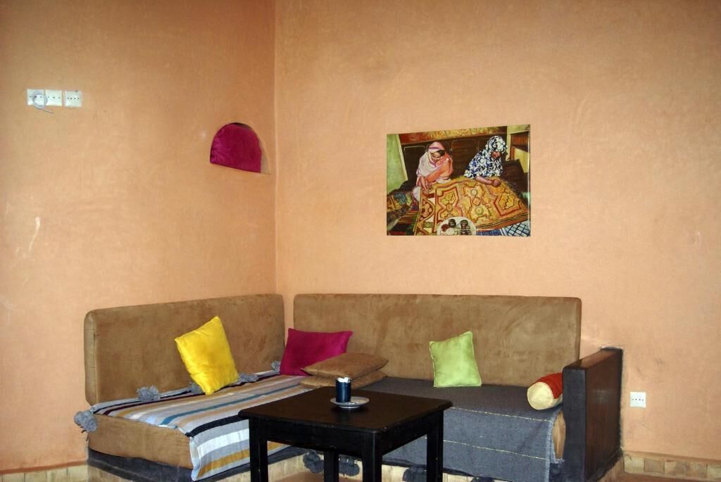 A room with a brown sofa, colorful cushions, a small table, and a wall-mounted picture.