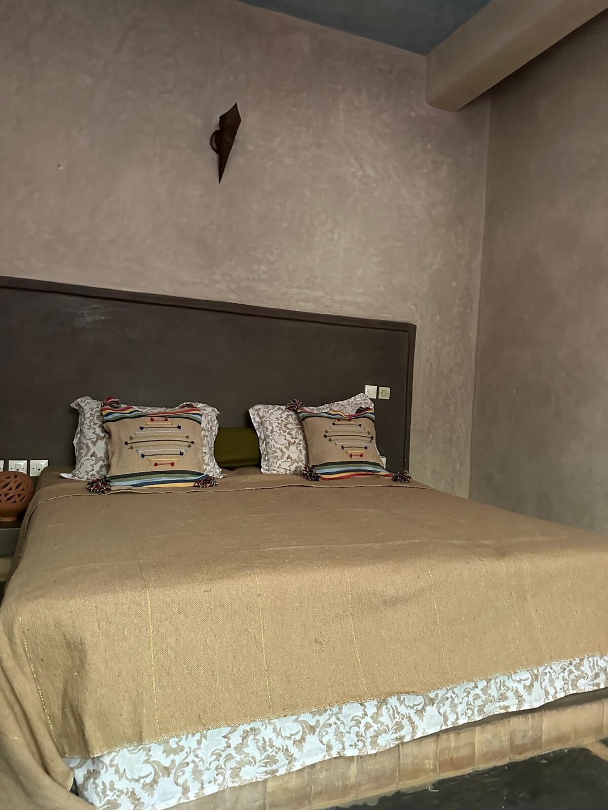 Un dormitorio con una cama grande, dos almohadas, un cabecero y una lámpara fijada a la pared.