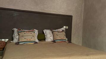 Un dormitorio con una cama grande, dos almohadas, un cabecero y una lámpara fijada a la pared.