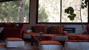 Una habitación acogedora con un sofá, una mesita y un banco. Se ve una ventana con vistas a árboles y una planta.