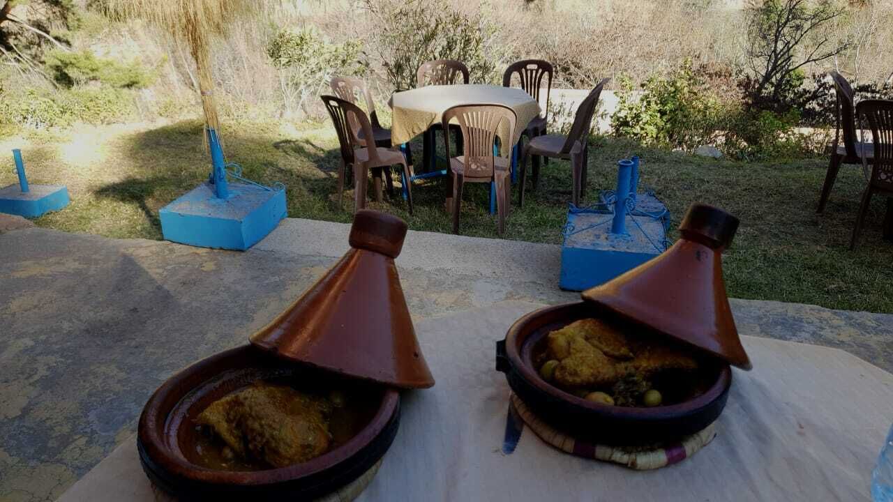 Dois tajines sobre uma mesa ao ar livre, com cadeiras e uma mesa ao fundo.