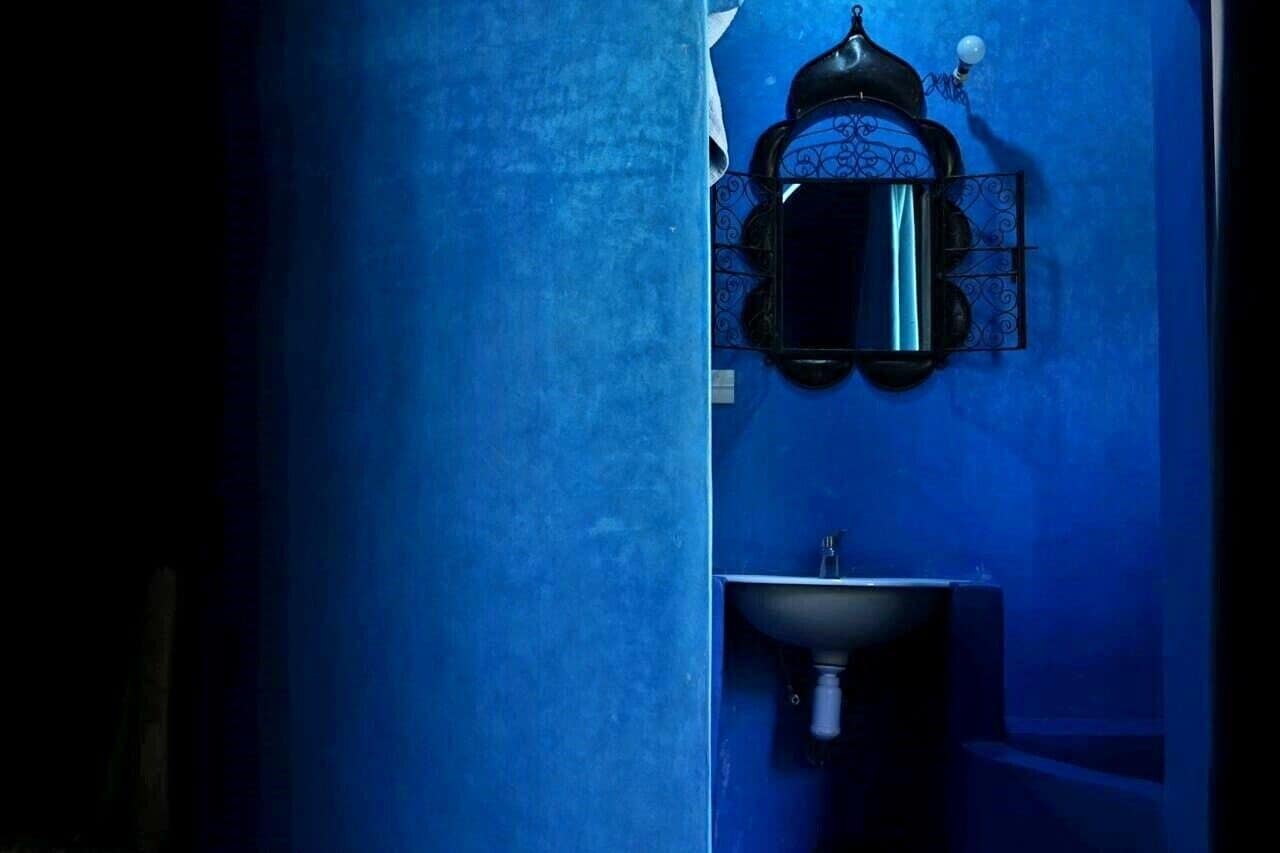 Un baño con pared azul, una cafetera negra y un lavamanos.