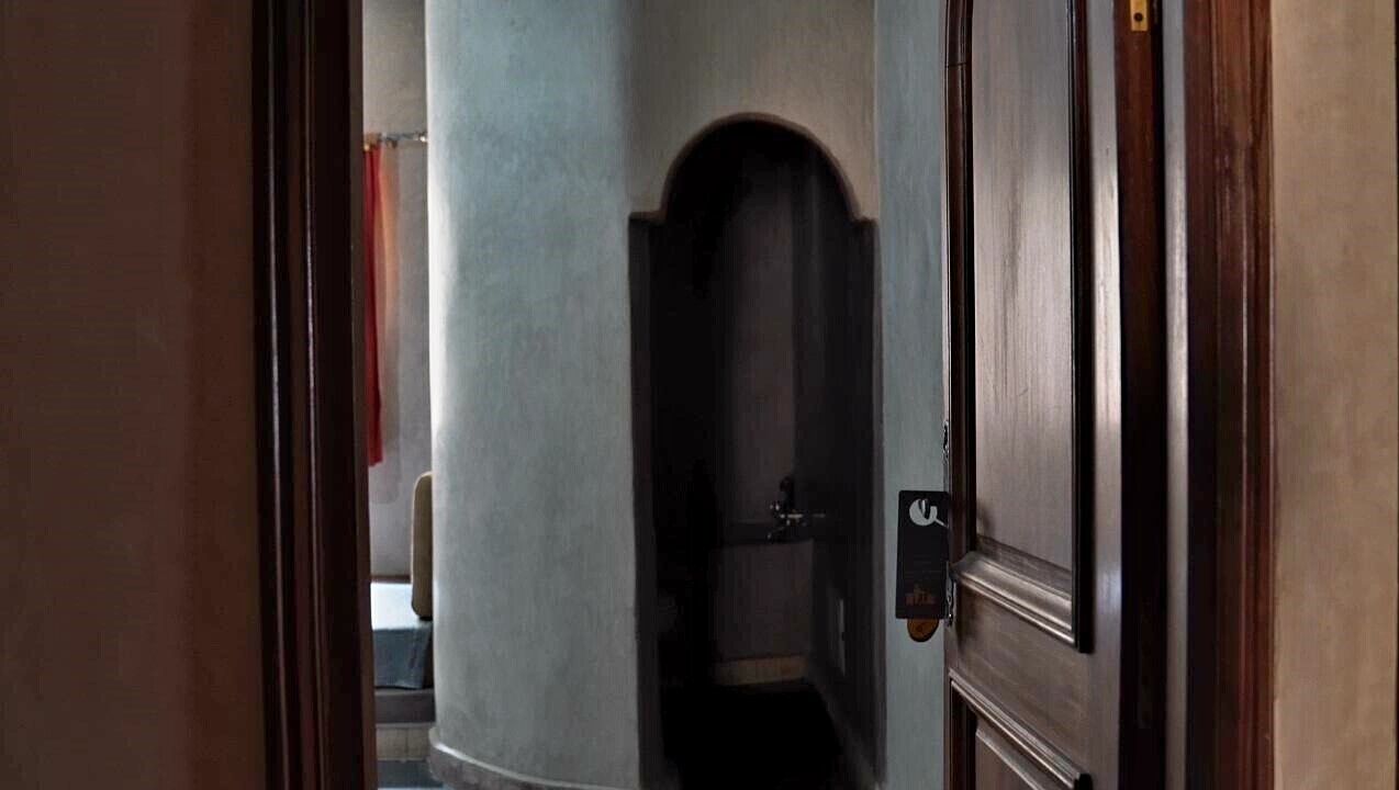 Un pasillo estrecho con una puerta de madera a la derecha y un pilar grande a la izquierda.