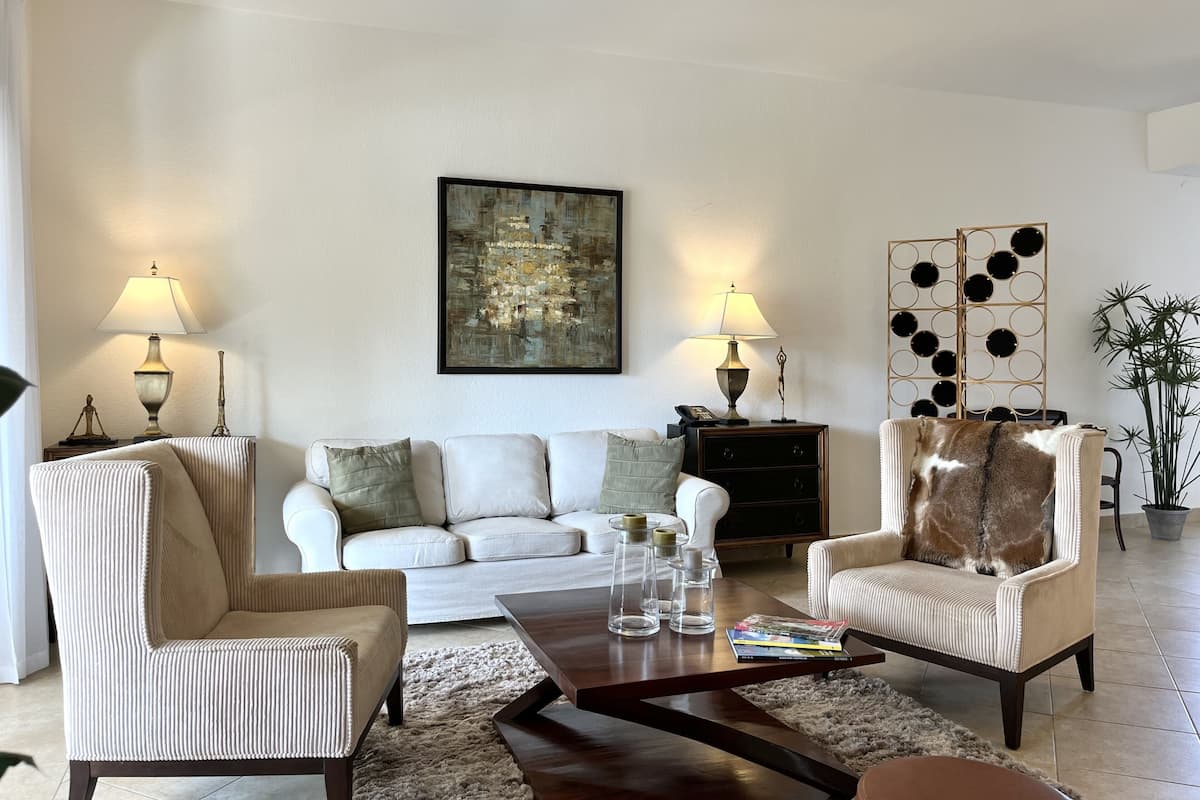 Ein Wohnzimmer mit Sofa, zwei Sesseln, einem Couchtisch, einer Lampe, einem Gemälde und einer Wanddekoration.