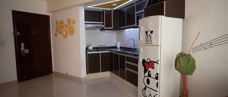 A modern kitchen with dark cabinets, a white refrigerator with cartoon designs, and a decorative plant.