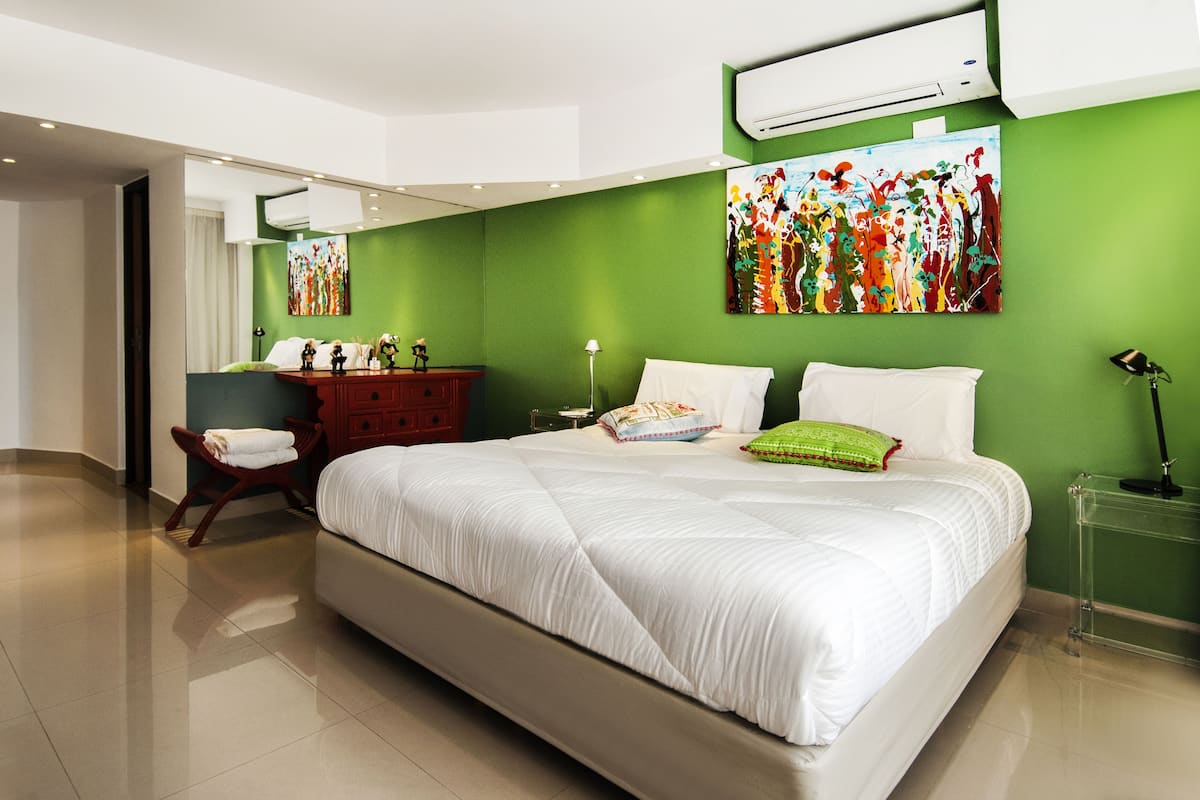 A modern hotel room with a large bed, green walls, and a large abstract painting.