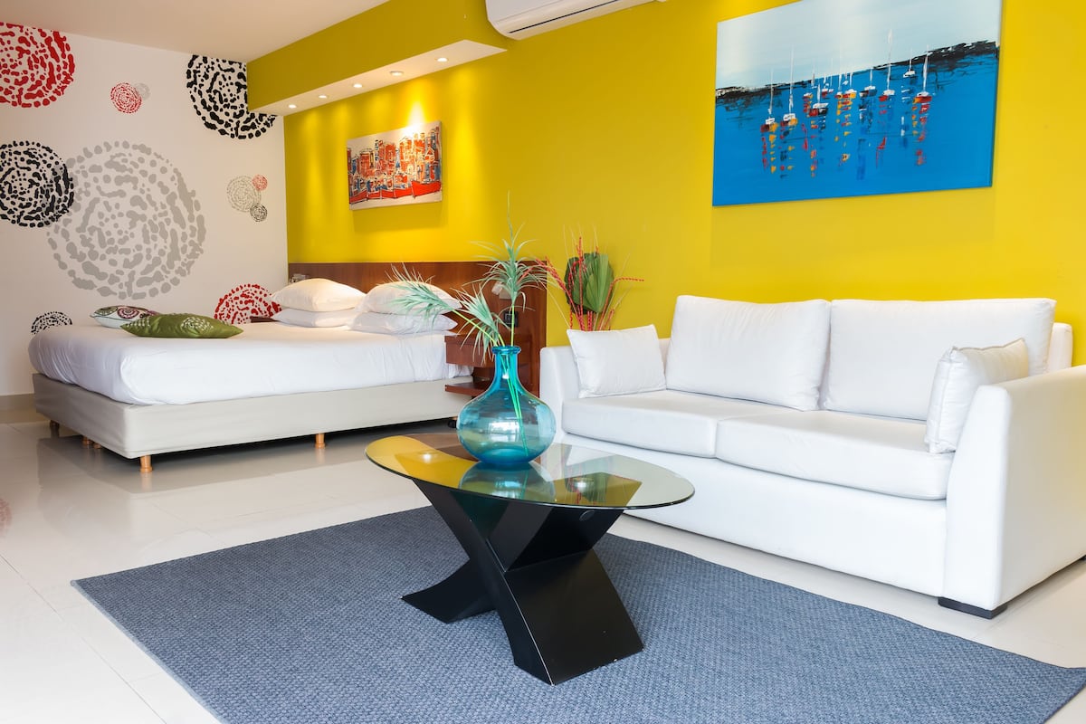 A modern living room with a white sofa, a glass coffee table, and a yellow accent wall.
