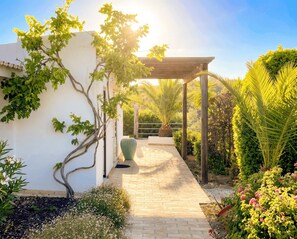 A garden pathway leading to a pergola with a white building on one side.