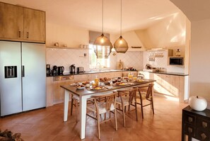 A modern kitchen with a central island, wooden chairs, and a dining table set for breakfast.