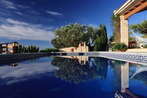 Una piscina con un riflesso limpido, circondata da alberi e un pergolato.