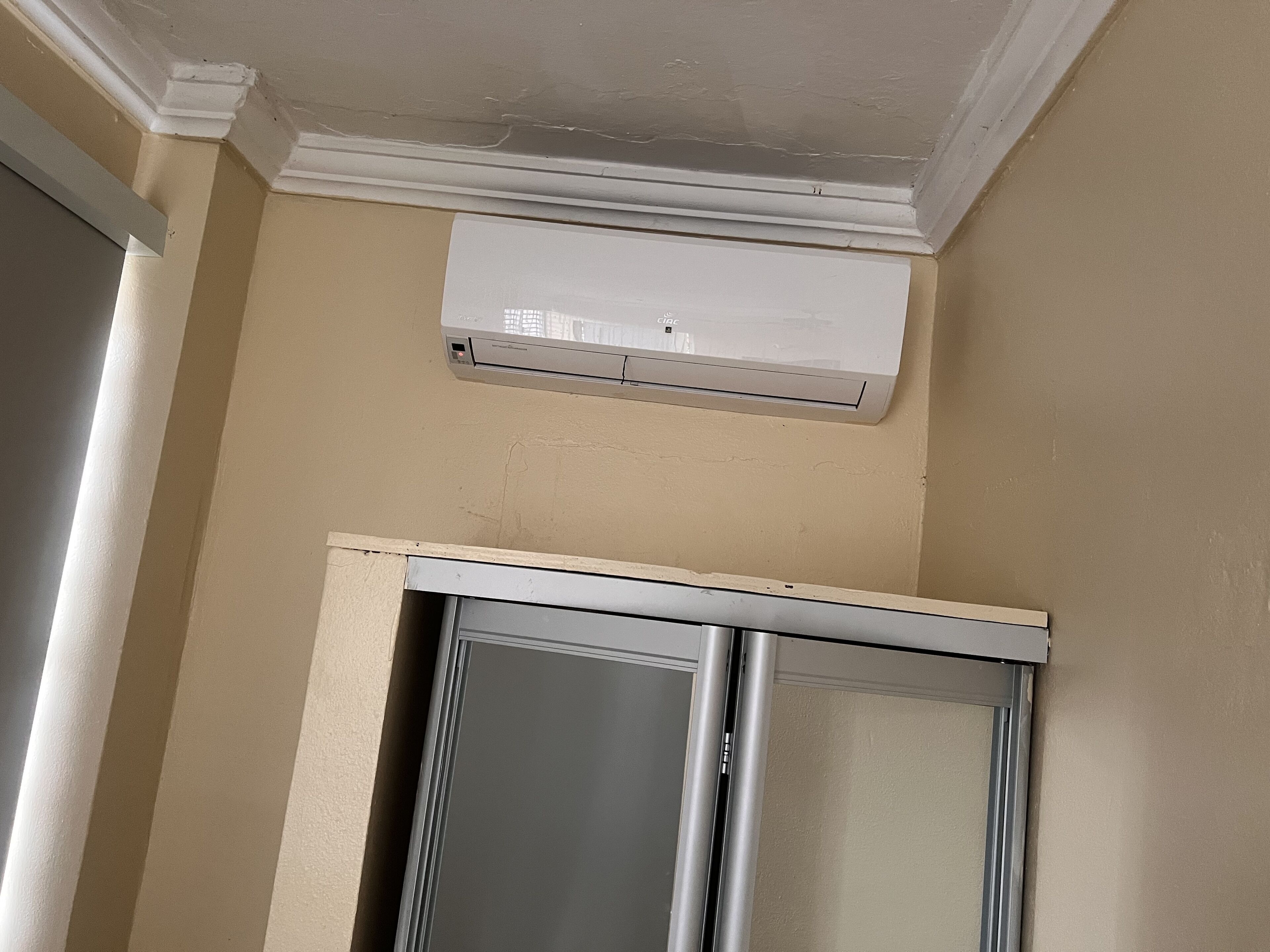 A room with beige walls, a white ceiling, and an air conditioning unit mounted on the wall.