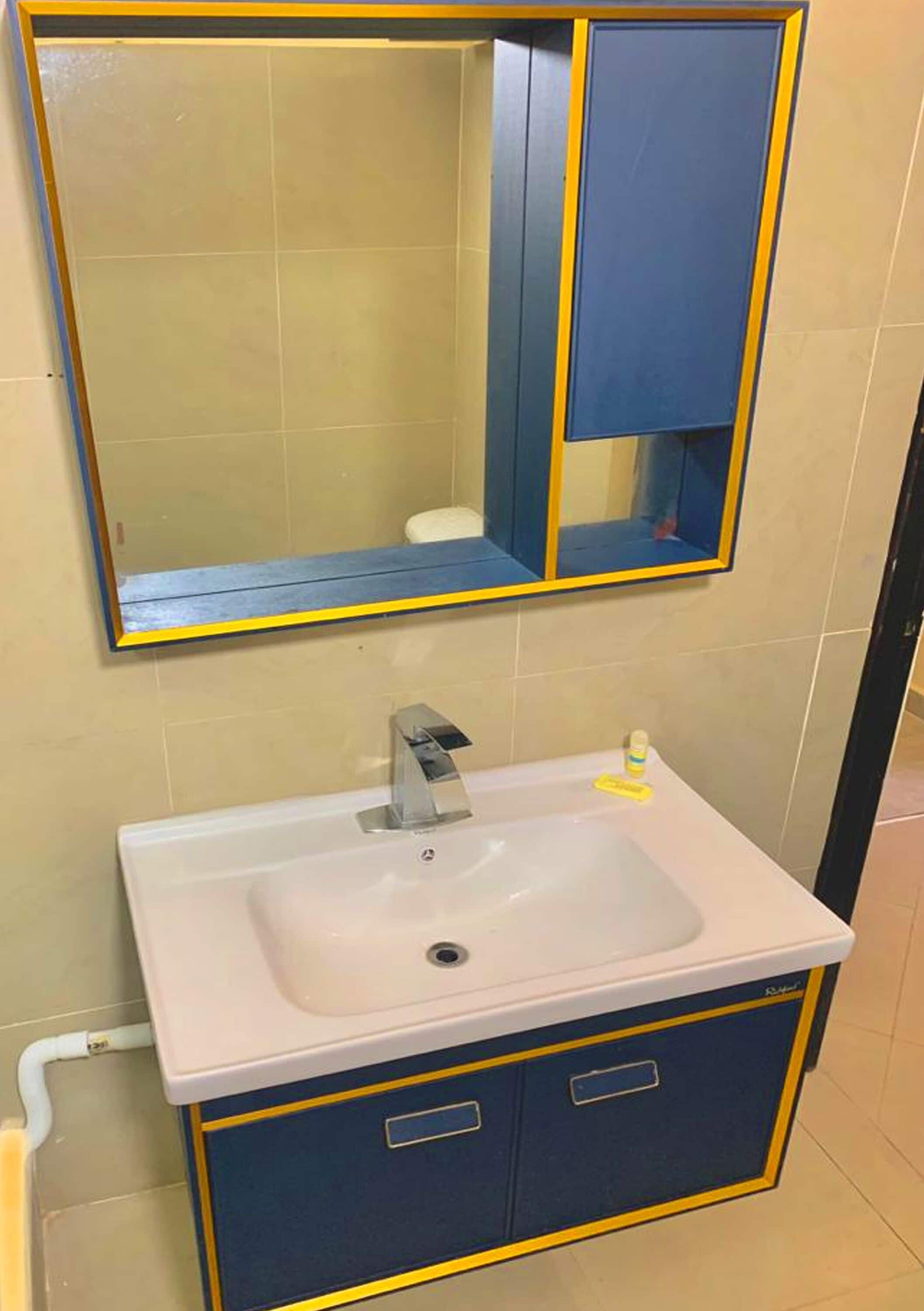 A bathroom with a white sink, a mirror with a blue frame, and a blue cabinet below the mirror.