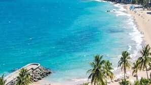 A coastal cityscape with a beach, clear blue waters, and high-rise buildings. - Hospedaje Primavera (San Juan)
