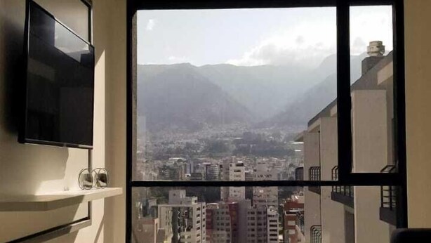 A modern apartment with a large window, a flat-screen TV, and two ottomans. - Luxury apartments Quito (Quito)